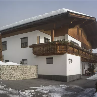 A cozy chalet in the snow with a traditional wooden balcony. The surroundings are wintry and peaceful.
