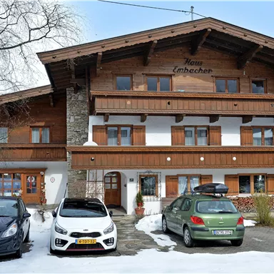 Ein traditionelles Chalet im alpinen Stil mit Holzverkleidung. Vor dem Gebäude stehen mehrere Autos und die Umgebung ist schneebedeckt.