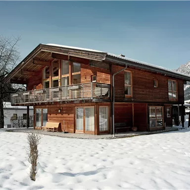 A pretty wooden house in a snowy landscape. Mountains can be seen in the background.