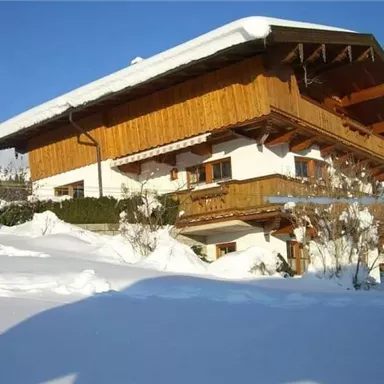 Ein gemütliches Holzhaus im Schnee, umgeben von einer winterlichen Landschaft. Der Himmel strahlt blau über dem schneebedeckten Boden.