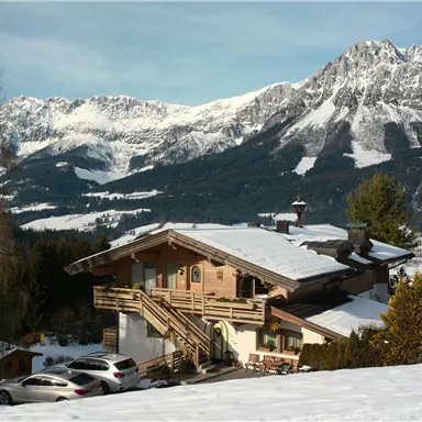 A alpine chalet covered in snow with majestic mountains in the background. The landscape radiates peace and idyllic charm.