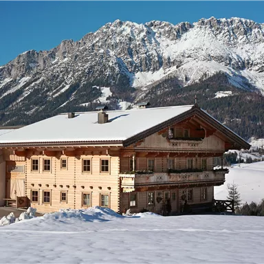 Ein charmantes Holzhhaus im Schnee mit beeindruckenden Bergen im Hintergrund. Die Landschaft ist winterlich und ruhig.