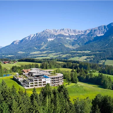 A modern hotel in the midst of a beautiful mountainous landscape. Green meadows and high mountains surround the accommodation.