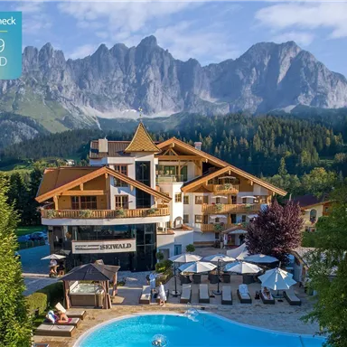 A hotel with a beautiful pool and surrounding loungers. In the background, majestic mountains rise under a clear sky.