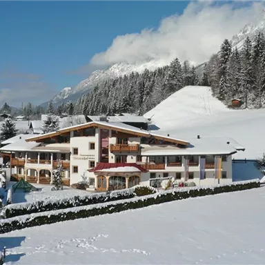 Ein schönes Hotel in den Alpen, umgeben von schneebedeckten Bergen. Die Landschaft ist winterlich und malerisch.