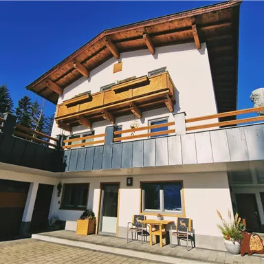 Ein modernes Haus mit einer Holz- und Metallfassade. Vor dem Haus steht ein Tisch mit Stühlen und es gibt einen klaren blauen Himmel im Hintergrund.