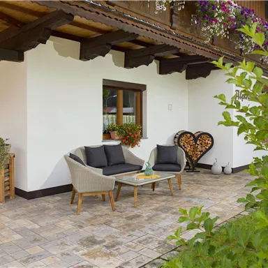A cozy outdoor area with comfortable furniture and a view of a green surroundings. The wall is decorated with blooming plants.