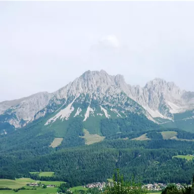 An impressive mountain landscape with high peaks and green meadows. The sky is slightly cloudy, giving the scene a tranquil atmosphere.