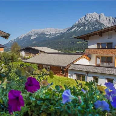 Ein malerischer Blick auf ein Hotel mit bunten Blumen im Vordergrund und majestätischen Bergen im Hintergrund. Der Himmel ist klar und blau.