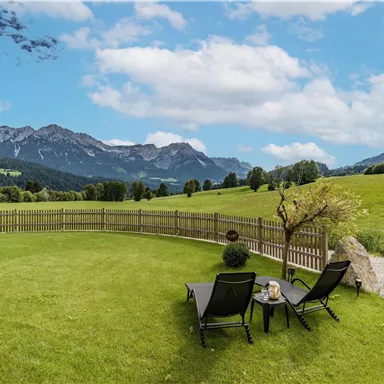 A beautiful meadow with two loungers and a view of the mountains. The sky is bright blue with some clouds.