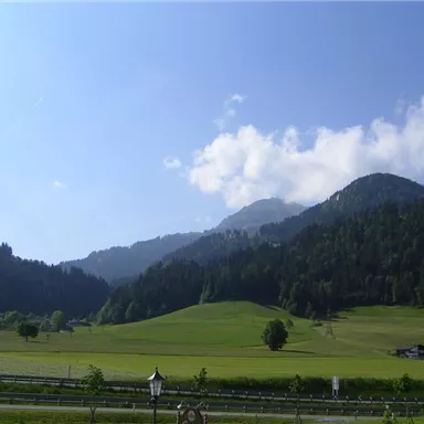 Eine malerische Landschaft mit sanften Hügeln und bewaldeten Bergen. Der Himmel ist blau und teilweise bewölkt, perfekt für einen entspannten Tag in der Natur.