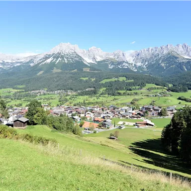 A picturesque mountain landscape with beautiful green meadows and a small village in the valley. The impressive mountains frame the scene.
