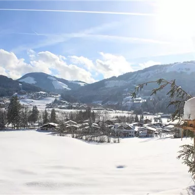 A snowy landscape with picturesque mountains in the background. The sun shines brightly over a small village that is nestled in winter's idyll.
