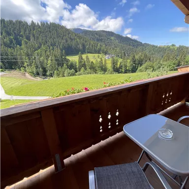 Ein schöner Ausblick von einem Balkon auf eine grüne Berglandschaft. Der Himmel ist blau mit wenigen Wolken.