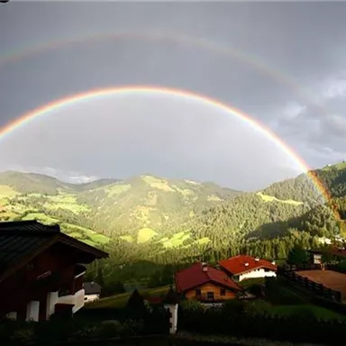 A beautiful rainbow over green hills and cottages. The sky is partly cloudy with rays of light illuminating the landscape.