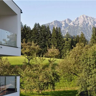 Eine moderne Wohnung mit einem Balkon blickt auf eine malerische Landschaft. Im Hintergrund erheben sich majestätische Berge und üppige Bäume.