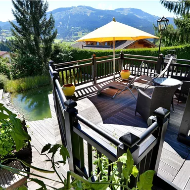 A cozy terrace with a view of the mountains. There are chairs and a sunshade on the terrace.