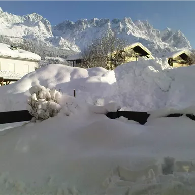 Eine verschneite Landschaft mit hohen Bergen im Hintergrund. Der Schnee bedeckt die Dächer und den Boden.