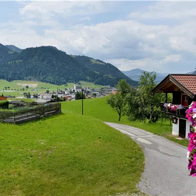 Eine malerische Landschaft mit sanften Hügeln und einem kleinen Dorf im Hintergrund. Blumen in leuchtenden Farben säumen den Weg.