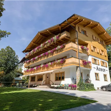 Ein charmantes Hotel mit Holzfassade und bunten Blumen. Umgeben von einem grünen Garten und Bäumen.