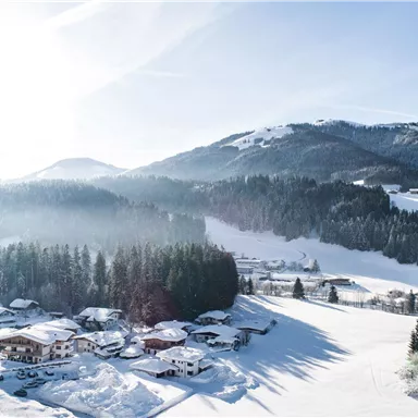 A picturesque winter landscape with snow-covered mountains and a small village. The sun shines brightly over the snowy fields.
