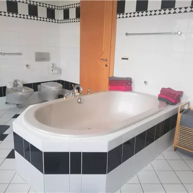A modern bathroom with a large bathtub and elegant black and white tiles. Towels in various colors are placed on a chair.