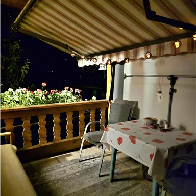 Ein einladender Balkon mit einem Tisch und Stühlen. Blumen sorgen für eine gemütliche Atmosphäre bei Nacht.