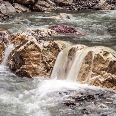 A flowing stream with slippery stones and gentle waterfalls. The surroundings feel natural and calm.