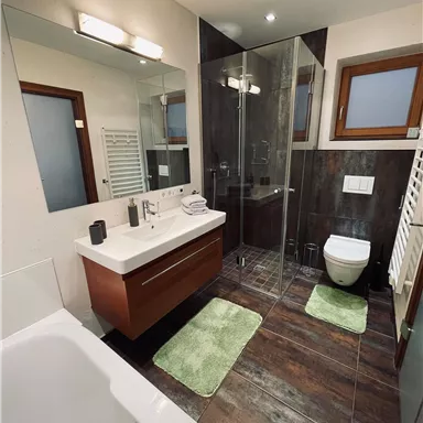 Ein modernes Badezimmer mit einer Dusche und einer Badewanne. Die Wände sind in neutralen Farben gehalten, und es gibt einen großen Spiegel und einen Waschplatz.