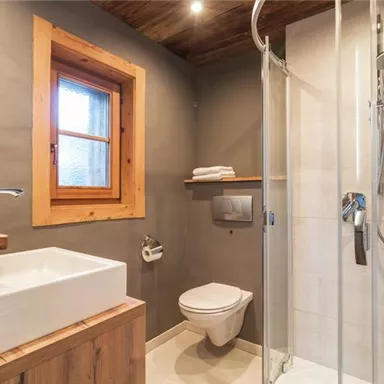 Ein modernes Badezimmer mit einer Dusche und einem eleganten Waschbecken. Das Holz und die helle Farbgestaltung schaffen eine einladende Atmosphäre.