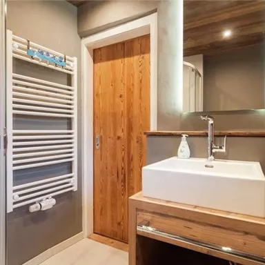 Ein modernes Badezimmer mit Holzdetails und einer stilvollen Waschbeckenanlage. Ein Handtuchheizkörper und eine warme Farbstimmung runden das Ambiente ab.