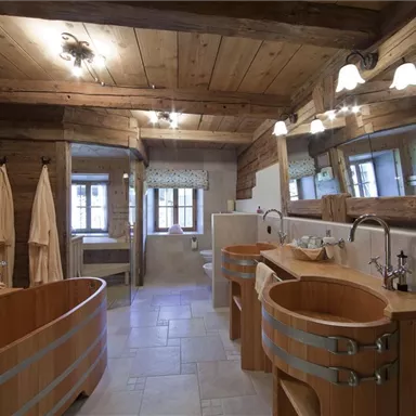 Ein modernes Badezimmer mit Holzdetails und zwei runden Holzbädern. Die Wände sind hell gefliest, und große Fenster sorgen für viel natürliches Licht.