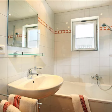 A modern bathroom with a bathtub and a sink. White tiles and a window ensure bright lighting conditions.