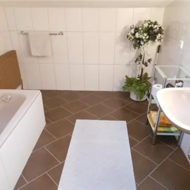 Ein modernes Badezimmer mit einer Badewanne und einem Waschbecken. Der Raum ist hell erleuchtet und mit Pflanzen dekoriert.