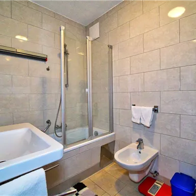 Ein modernes Badezimmer mit Fliesen und einer Dusche. Es gibt ein Waschbecken, eine Toilette und Handtücher.