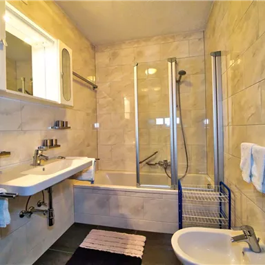 Ein modernes Badezimmer mit einer Badewanne und einer Dusche. Die Wände sind mit hellen Fliesen versehen, und es gibt eine Waschbecken mit Spiegel.