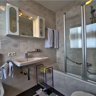 Ein modernes Badezimmer mit einer Dusche und Badewanne. Es sind Handtücher und Pflegeprodukte sichtbar.