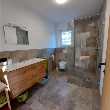 Ein modernes Badezimmer mit einer gläsernen Dusche und einem Holzwaschbecken. Weiße Wände und gut beleuchtet, mit einem schicken, klaren Design.