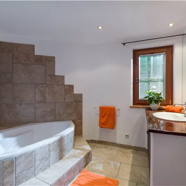 A modern bathroom with a comfortable bathtub and a stylish sink. Orange towels and plants provide an inviting accent.