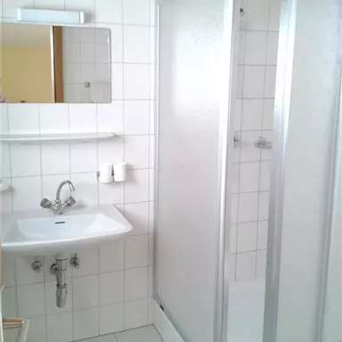 A modern bathroom with a shower cabin and a sink. The walls are tiled, and there is a mirror above the sink.