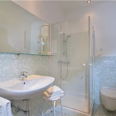 Ein modernes Badezimmer mit einer Duschkabine und einem Waschbecken. Die Wände sind in sanften Farben gefliest und es gibt frische Handtücher.