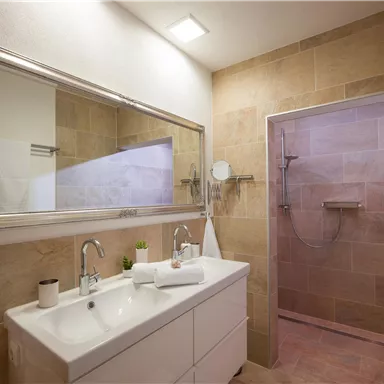 A modern bathroom with a double sink and a large mirror. The beige tiles and the shower create an inviting atmosphere.