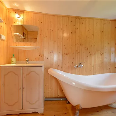 Ein gemütliches Badezimmer mit Holzvertäfelung. Die freistehende Badewanne und der Waschtisch verleihen dem Raum einen rustikalen Charme.