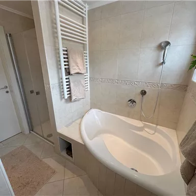 Ein modernes Badezimmer mit einer ovalen Badewanne und einem Duschbereich. Eingerichtet mit hellen Fliesen und einer Pflanze am Fenster.