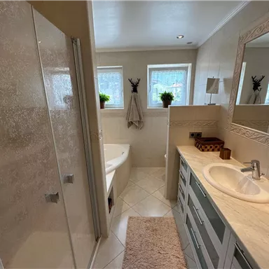 Ein modernes Badezimmer mit einer klaren Duschkabine und einer Badewanne. Das Waschbecken ist elegant gestaltet und es gibt Pflanzen auf den Fensterbänken.