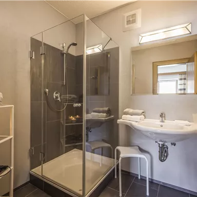 A modern bathroom with a glass shower and a sink. Towels and decoration are placed on a shelf.