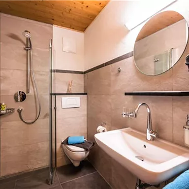 A modern bathroom with a shower and sink. The walls are in neutral colors, and there are towels and toiletries.