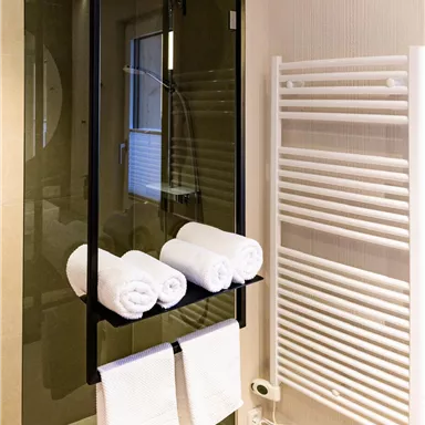 A modern bathroom with a glass shower and a towel rack. White towels are neatly lined up.