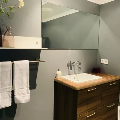 A modern bathroom with a simple sink and a wooden base. White towels hang next to a mirror on the wall.