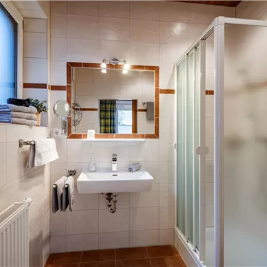 A modern bathroom with a shower and a sink. The walls are tiled in light colors and there is a large window.